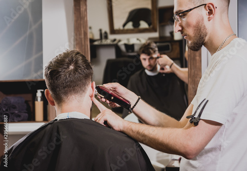 Young man with trendy haircut at barber shop. Barber does the hairstyle and beard trim.