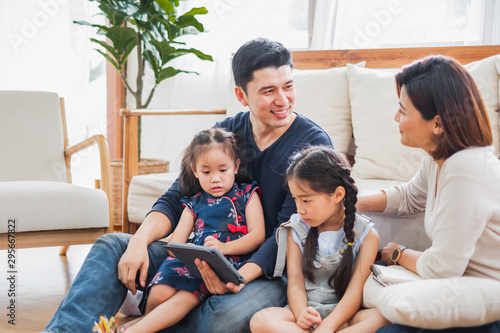 Happy Asian family using tablet, laptop for playing game watching movies, relaxing at home for lifestyle concept