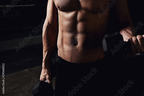 Man on a dark background with dumbbells in his hands.