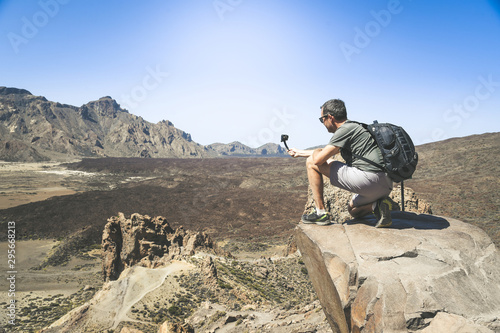 Travel blogger with backpack making video with action cam for social blog. Caucasian man taking pictures on a mountain cliff overlooking the lavic panorama. Holiday, travel, new trend tech concept. photo