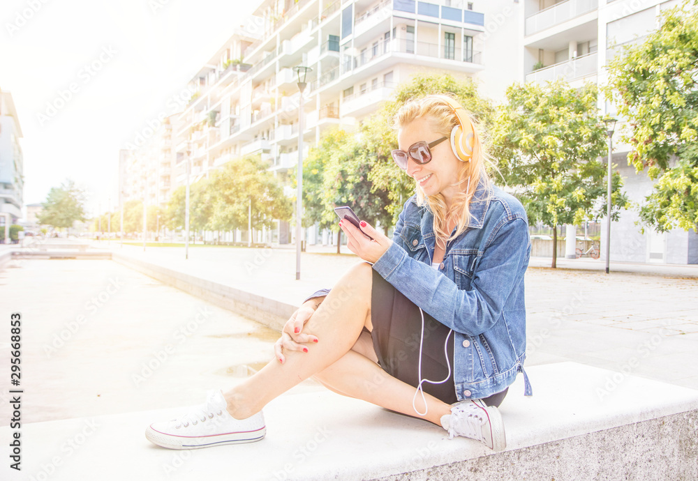 beautiful blond woman is listening music with headphone in a sunny day