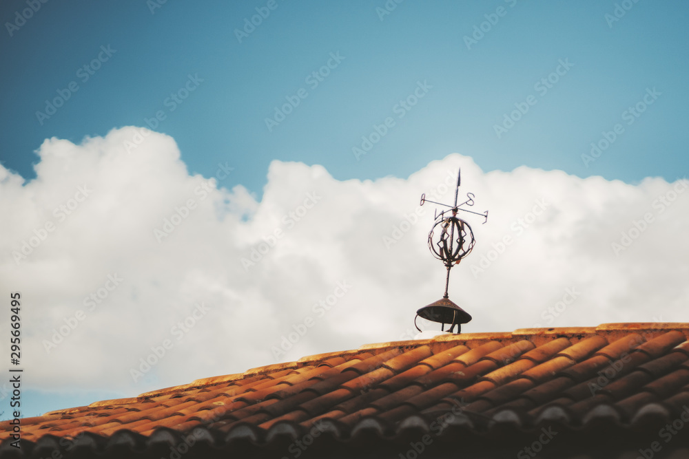 Minimalistic shot of an antique tiled roof of some residential house in Europe with an old rusty weather rickety vane on the top and a beautiful cloudscape in a defocused background Minimalistic shot of an antique tiled roof of some residential house in Europe with an old rusty weather rickety vane on the top and a beautiful cloudscape in a defocused background