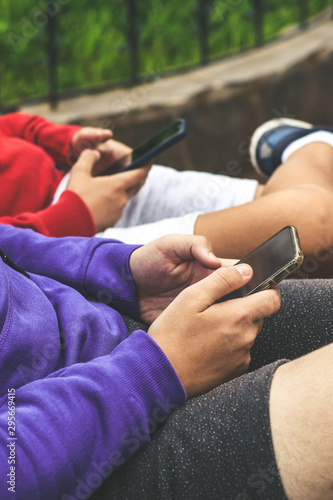 Close up view of a couple of teen using smartphone sitting outdoor at the park. Teenagers communicate with new technology devices with remote friends. Youth, new tech trend and communication concept.