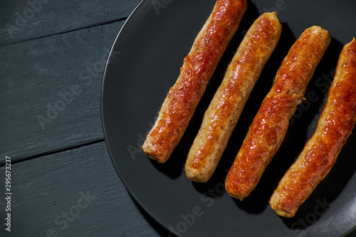 Grilled sausage on plate over dark wooden background.