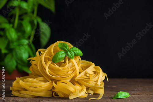raw fettuccine pasta heap and fresh basil leaf on wooden dark background copy space