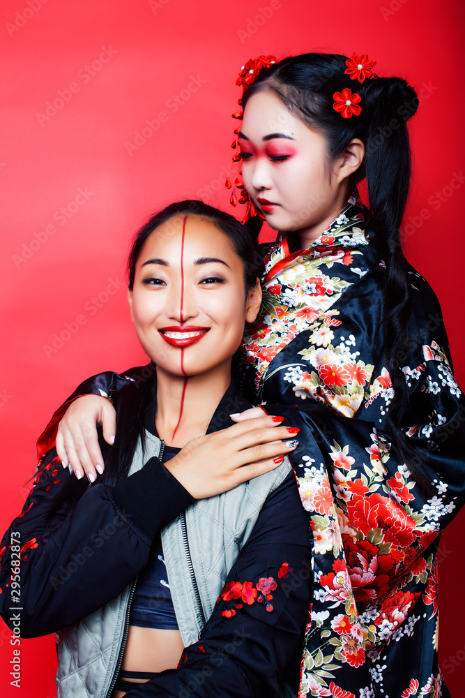 two pretty geisha girls friends: modern asian woman and traditional wearing kimono posing cheerful on red background two pretty geisha girls friends: modern asian woman and traditional wearing kimono posing cheerful on red background