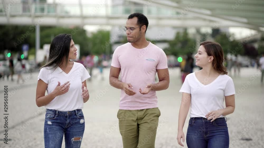 Smiling relaxed friends walking on street and talking. Front view of cheerful young people having pleasant conversation during stroll. Communication concept Smiling relaxed friends walking on street and talking. Front view of cheerful young people having pleasant conversation during stroll. Communication concept