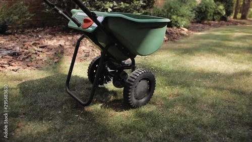 Man fertilizing and seeding residential backyard lawn with manual grass fertilizer spreader.