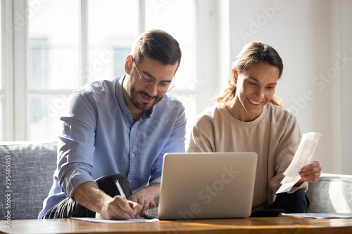 Happy couple using laptop, calculating domestic bills, mortgage documents