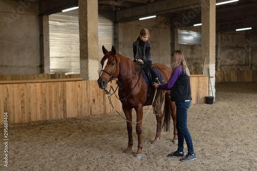 a little girl learning to sit astride a horse in the background of an old stable . indoor riding lessons