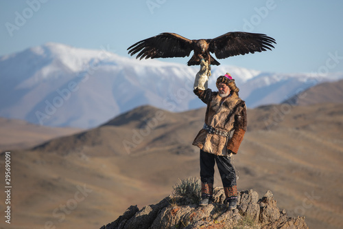 Old traditional kazakh eagle hunter posing with his golden eagle in the mountains. Ulgii, Western Mongolia.