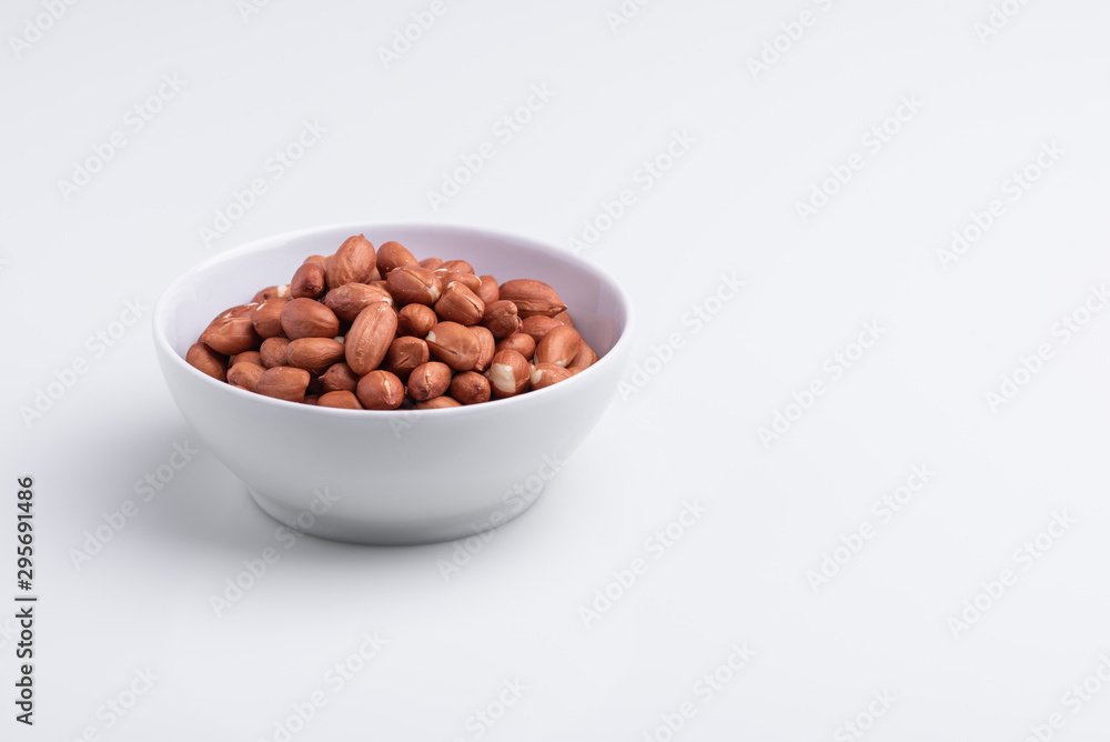 Raw shelled whole peanuts in a white bowl, isolated on white background, soft light, copy space Raw shelled whole peanuts in a white bowl, isolated on white background, soft light, copy space