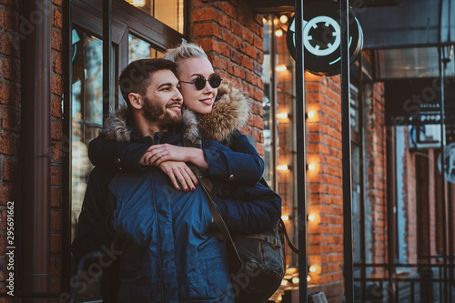 Attractive blond woman in sunglasses is hugging her handsome man on the street.