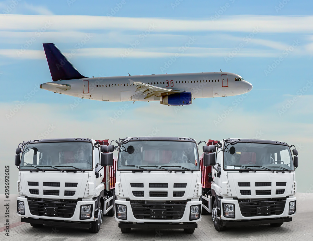 Three trucks are frontal front view and the plane is flying in the sky
