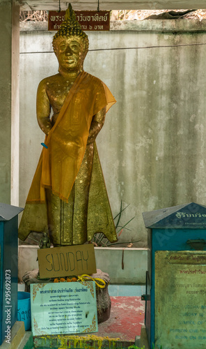 Bang Saen, Thailand - March 16, 2019: Wang Saensuk Buddhist Monastery. Gilded Buddha Image statue representing Sunday is standing bodhisattva. Blue bucket and collection box. photo