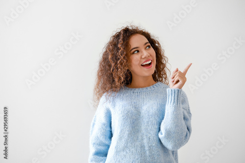 Portrait of young African-American woman pointing at something on light background