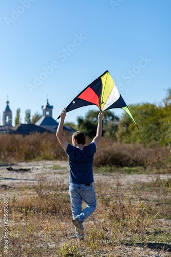 A man  in a black T-shirt launches a blue kite into a cloudless sky. The concept of freedom, summer hobbies, entertainment in nature. Minimalism, space for text, shades of blue
