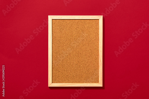 Empty cork board with wooden frame on red background, view from above with place for text.