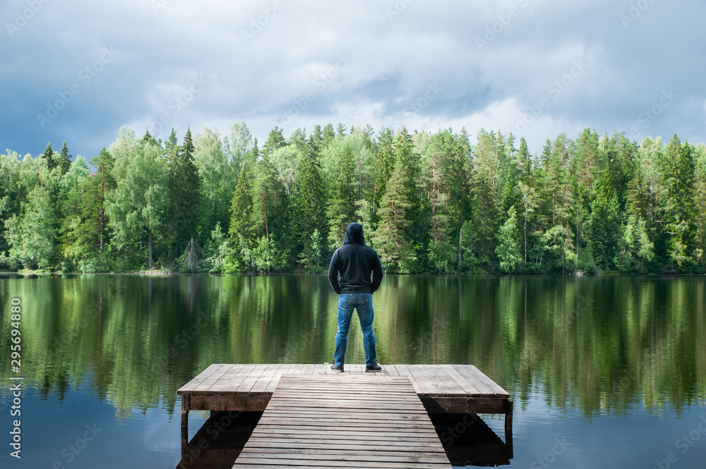 Man stands on the pier of a beautiful lake, panoramic photo. The concept of freedom and independence, a symbolic photo of the beauty of nature