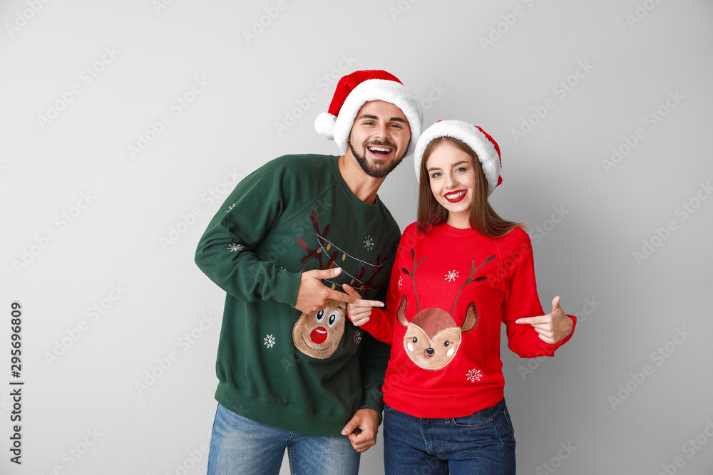 Happy young couple in Christmas clothes on light background Happy young couple in Christmas clothes on light background