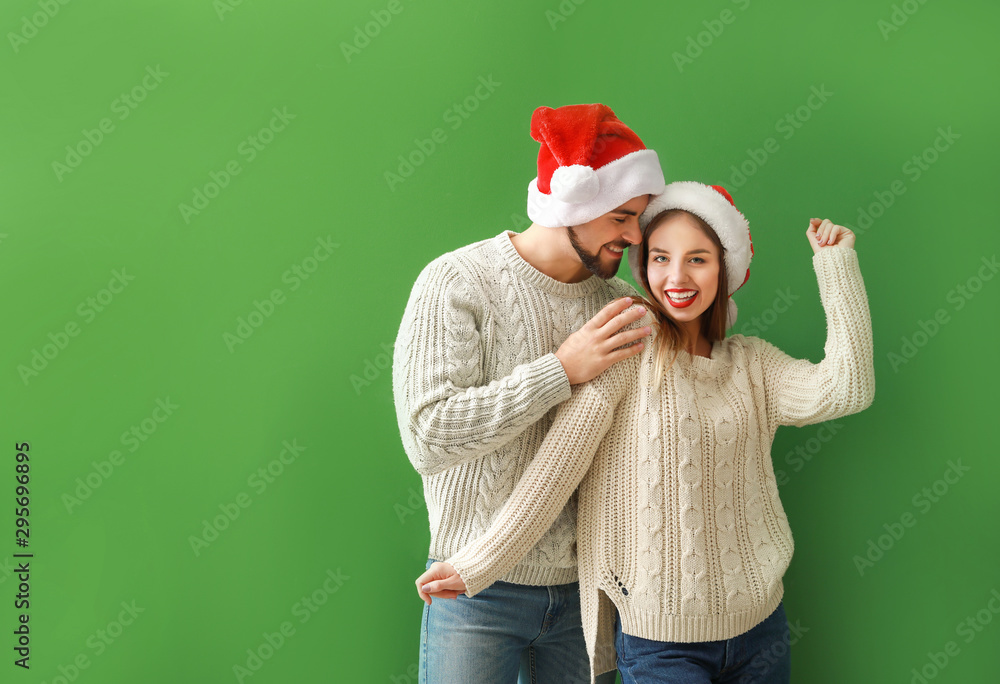 Happy young couple in Santa hats on color background Happy young couple in Santa hats on color background