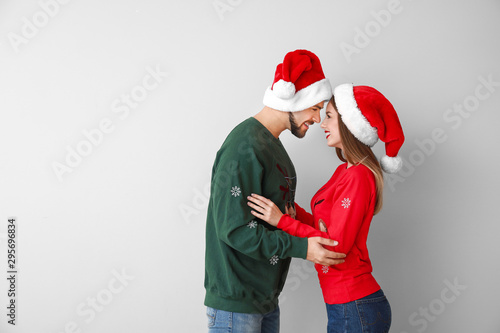 Happy young couple in Christmas clothes on light background
