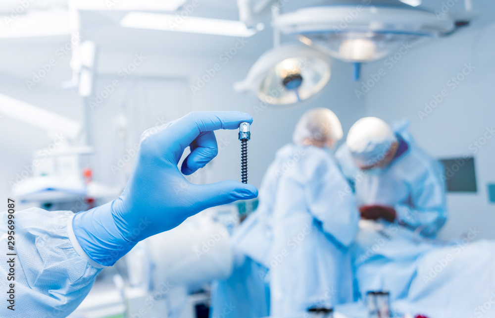 Fototapeta premium Spinal surgery. Surgeon show polyaxial screw in operating room with surgery equipment. Laminectomy. Spine fixation systems