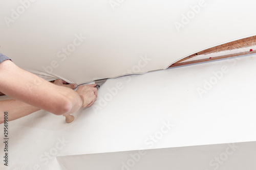 Rapairman istalling a stretch ceiling made of pvc vinyl using a special tool.