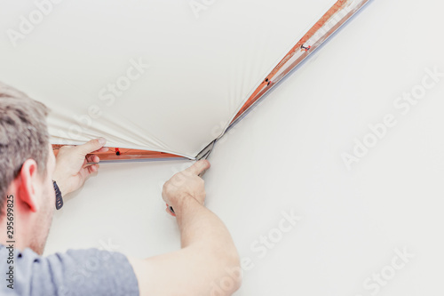 Repairman installing stretch ceiling with a special tool in the room.