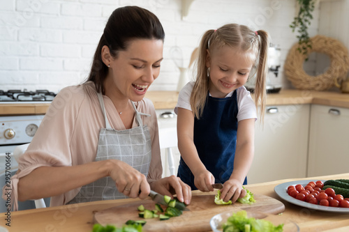 Happy mother and little daughter wearing apron cooking together