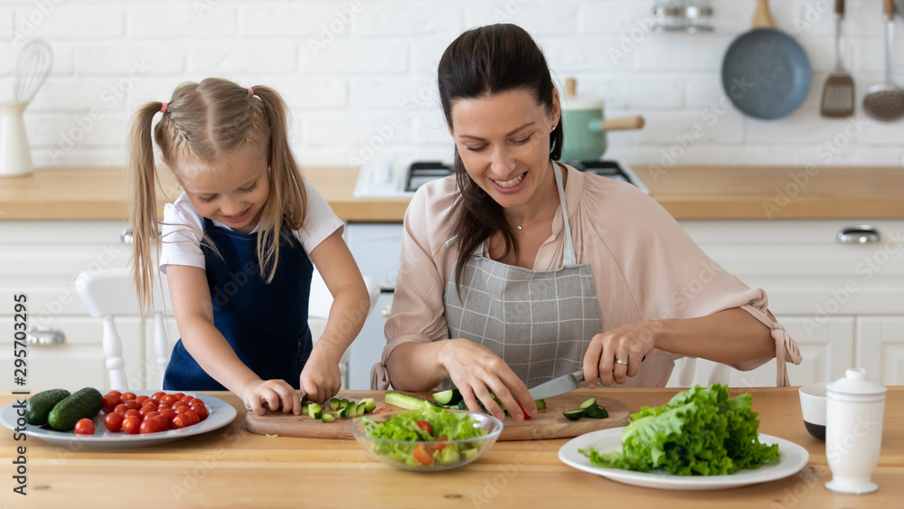 Smiling mother and little daughter cooking salad together in kitchen Smiling mother and little daughter cooking salad together in kitchen