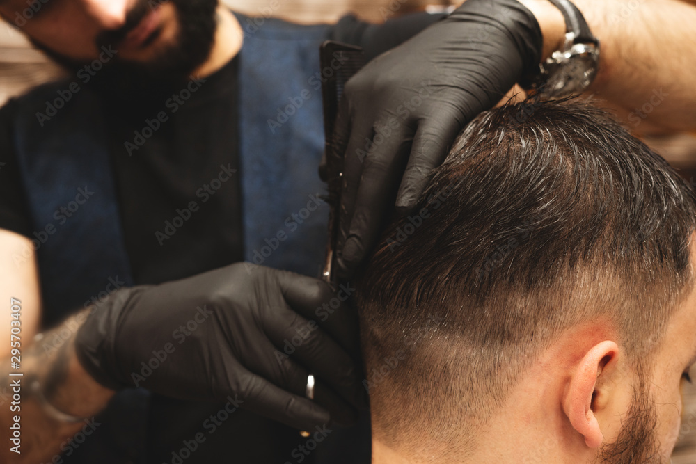 Fototapeta premium Haircut head in barbershop. Barber cuts the hair on the head of the client. The process of creating hairstyles for men. Barber shop. Selective focus.