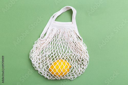 Mesh shopping bag with lemons on green canvas background. reusable concept. BACK TO NATURE