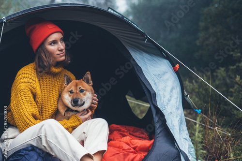 tourist traveler in camp tent hugging red shiba inu on background foggy rain forest, hiker woman with puppy dog in mist nature trip, friendship love concept, relax girl resting dog together