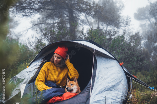 tourist traveler hugging red shiba inu in camp tent on background foggy rain forest, hiker woman with puppy dog in mist nature trip, friendship love concept