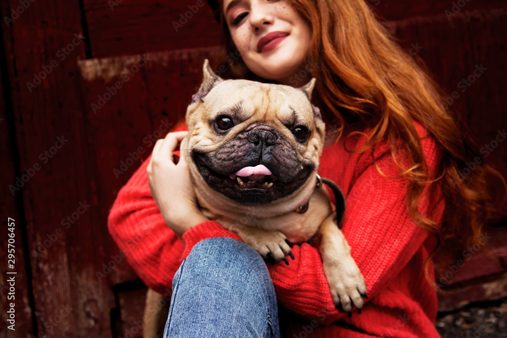 Happy owner of bulldog is hugging witn the dog and have fun outdoor. Woman wearing orange sweater and jeans.