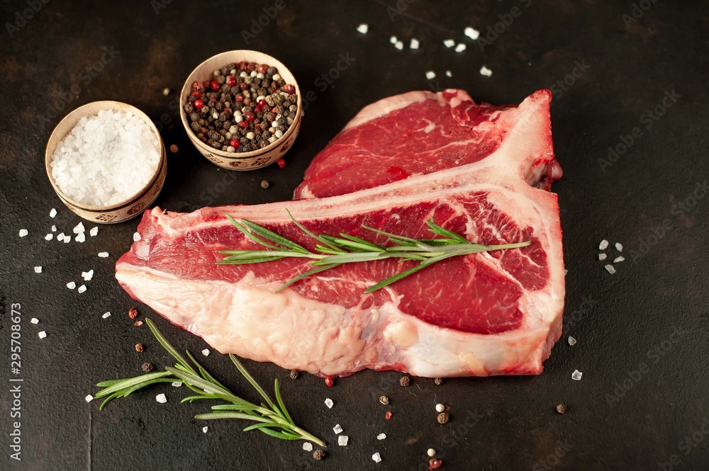 Raw t-bone steak with fresh herbs on a concrete or slate background, top view