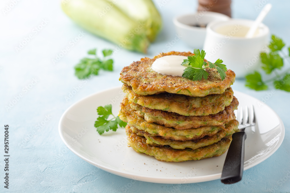 Zucchini fritters with fresh parsley and sour cream in plate on blue concrete background. Selective focus.