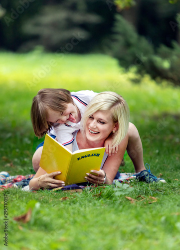 Mother and son playing fools while reading on a rug amidst a summer park lawn