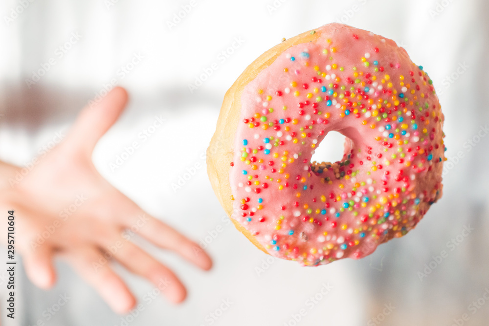 Hand throws and catches a pink donut with icing pastry topping