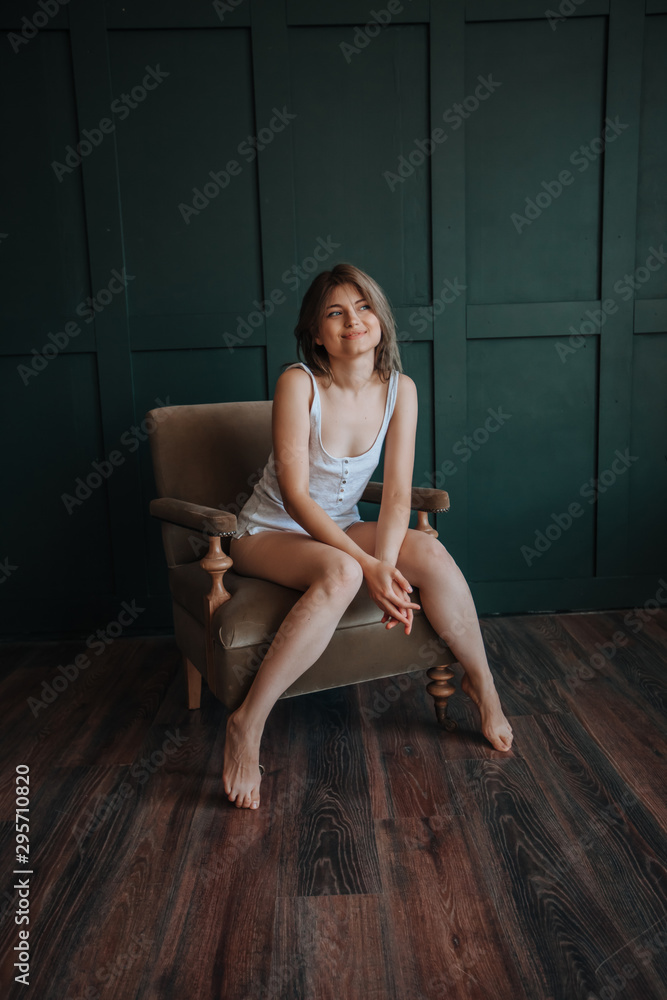 Beautiful girl with long thin legs sitting on a chair on a dark green background Beautiful girl with long thin legs sitting on a chair on a dark green background