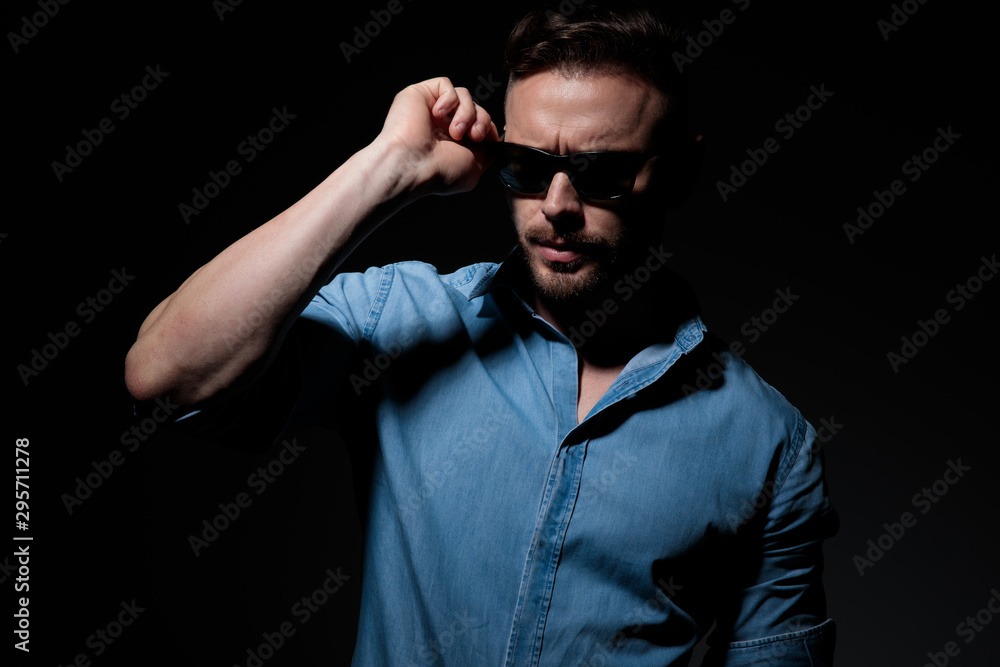 Obraz premium casual man standing and fixing sunglasses with strong attitude
