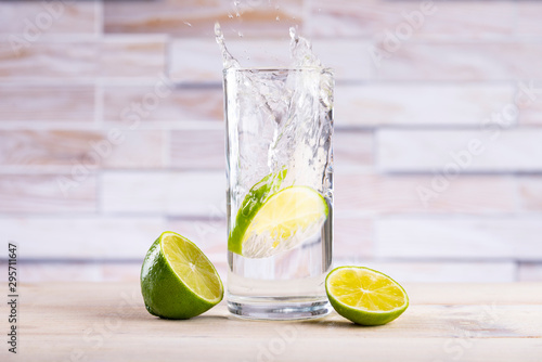 A slice of lemon falls into a glass with water, splashes fly on a wooden table