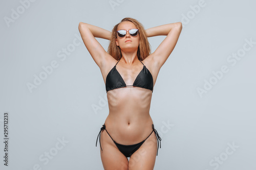 Girl in a black swimsuit and sunglasses on a light gray background © Smeilov