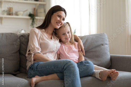 Happy young mother hugging little daughter, sitting on couch together