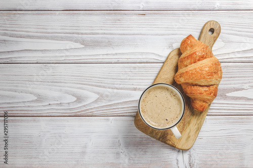 Croissants on a wooden board and cappuccino on white wooden table. French breakfast. Copy space. Top view. Flat lay