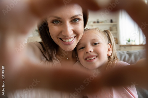 Happy mother and little daughter taking selfie, showing heart sign