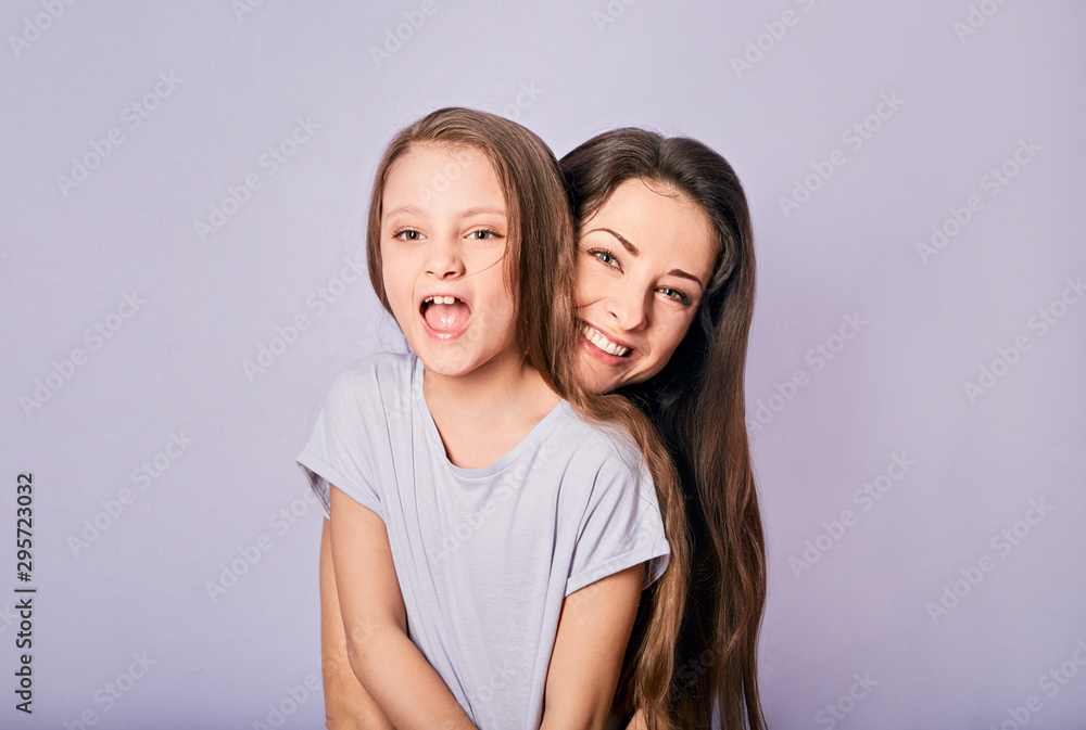 Happy excited cuddling mother and daughter shouting with wide opened mouth on purple background with empty copy space. Happy excited cuddling mother and daughter shouting with wide opened mouth on purple background with empty copy space.