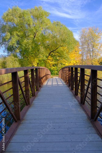 Wooden bridge with metal rails on water with beautiful fall colors on a sunny day