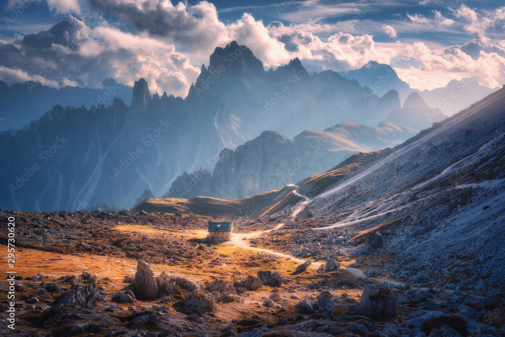 Small house in beautiful mountain valley, orange grass, stones, blue sky with clouds at sunset in autumn. Colorful landscape with building, mountains. Tre Cime park in Dolomites, Italy. Alps in fall - obrazy, fototapety, plakaty 